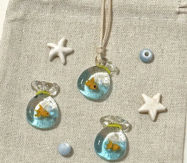 Women's necklace with a blue hand-painted fish charm on a beige cotton and linen clavicle chain.