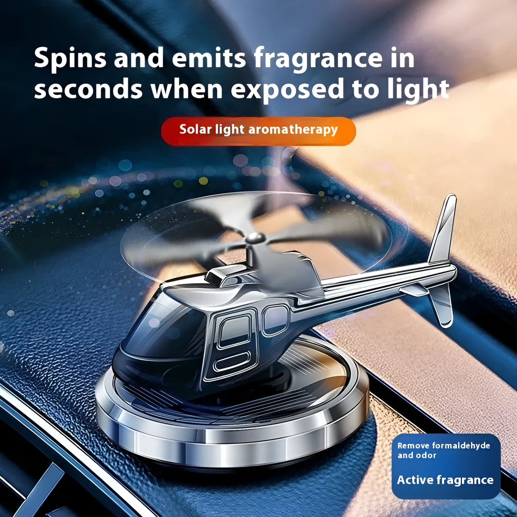 Silver metal solar-powered helicopter car air freshener clipped to a vehicle air vent, with rotating blades.