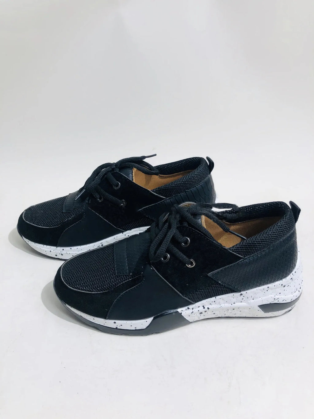 Women's black suede wedge sneakers with a low-cut ankle and round toe on a wooden floor.