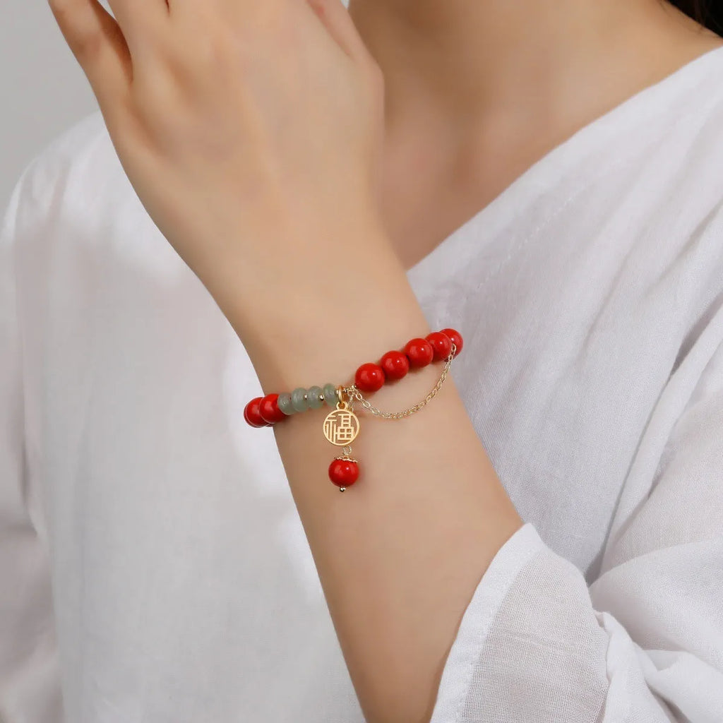 Women's red cinnabar bracelet with fu character charm, jade spacer bead, and tassel design