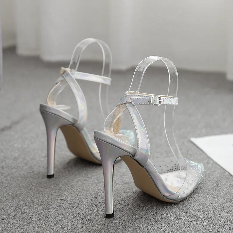 Women's pointed toe stiletto sandals with a diamond embellishment on the PVC upper and an adjustable ankle strap.