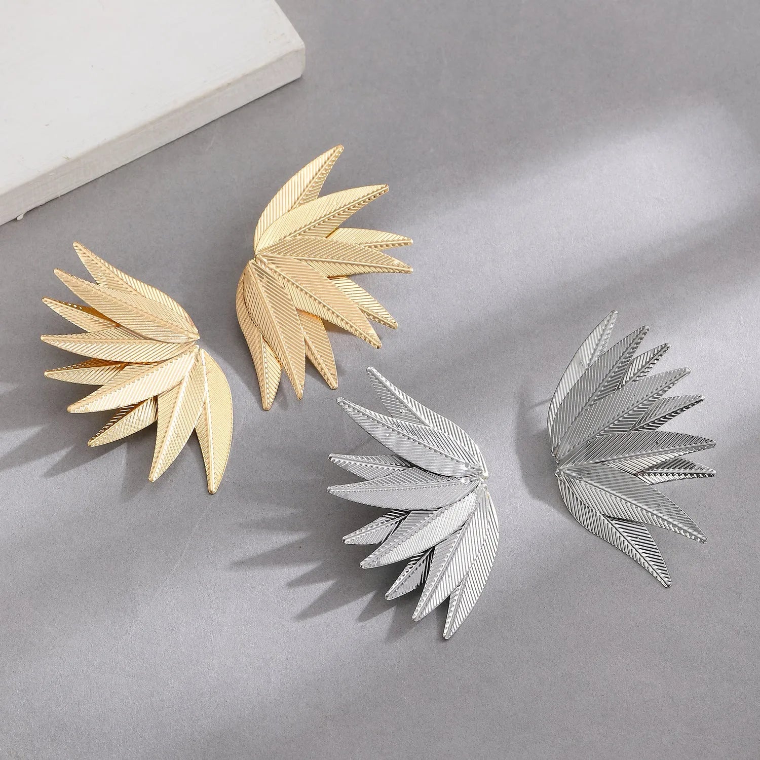 Gold and white alloy leaf-shaped patch earrings on a plain background