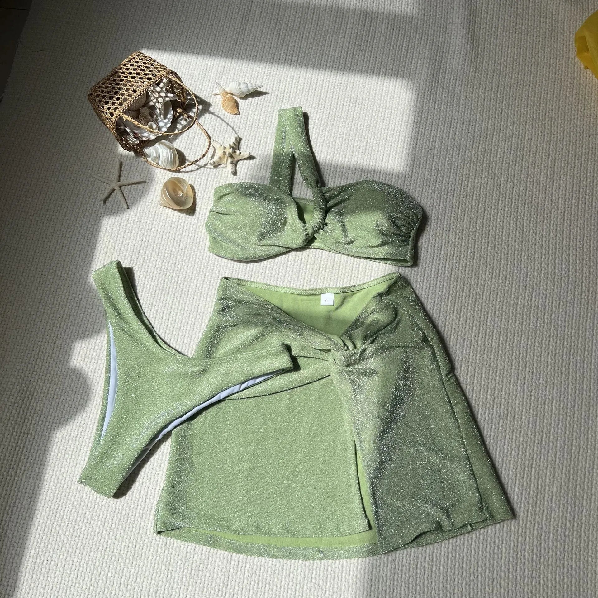 Women's light green one-shoulder glossy polyester three-piece swimsuit set on a hanger.