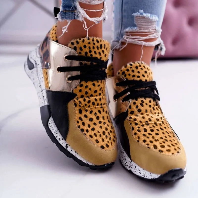 Women's black suede wedge sneakers with a low-cut ankle and round toe on a wooden floor.