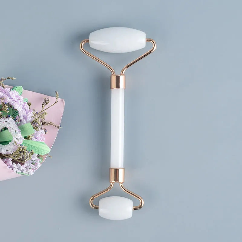 White jade facial roller and gua sha scraping board set on a table.
