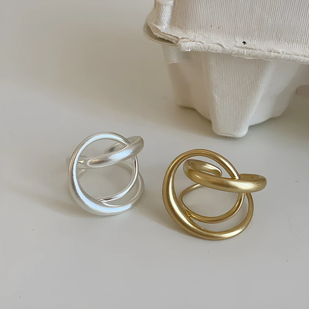 Geometric open ring with interlaced metal design and matte finish in gold colour.