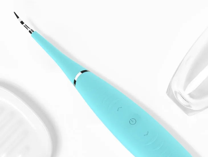 Pink and blue waterproof electric dental scaler tool on a bathroom counter with charging cable.