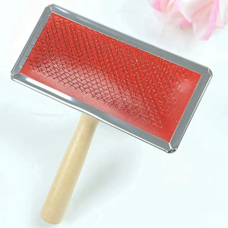 Red pet needle comb with wooden handle and stainless steel pins on a grooming surface