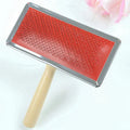 Red pet needle comb with wooden handle and stainless steel pins on a grooming surface