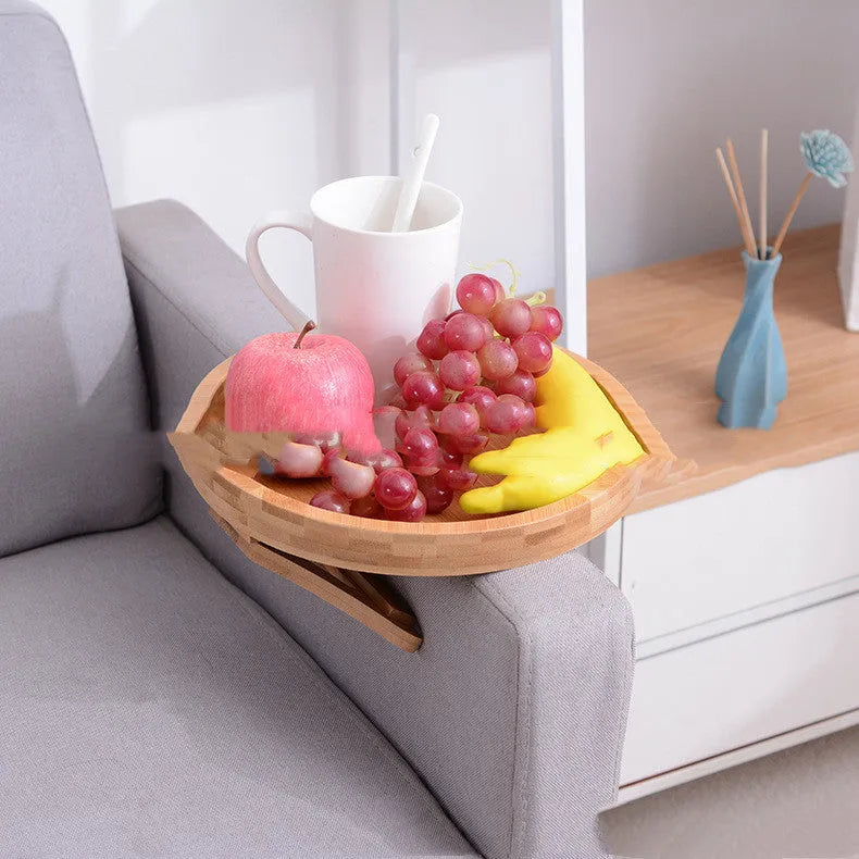 Wooden clip-on sofa tray table with carved surface in bamboo colour, attached to armrest holding snacks and remote