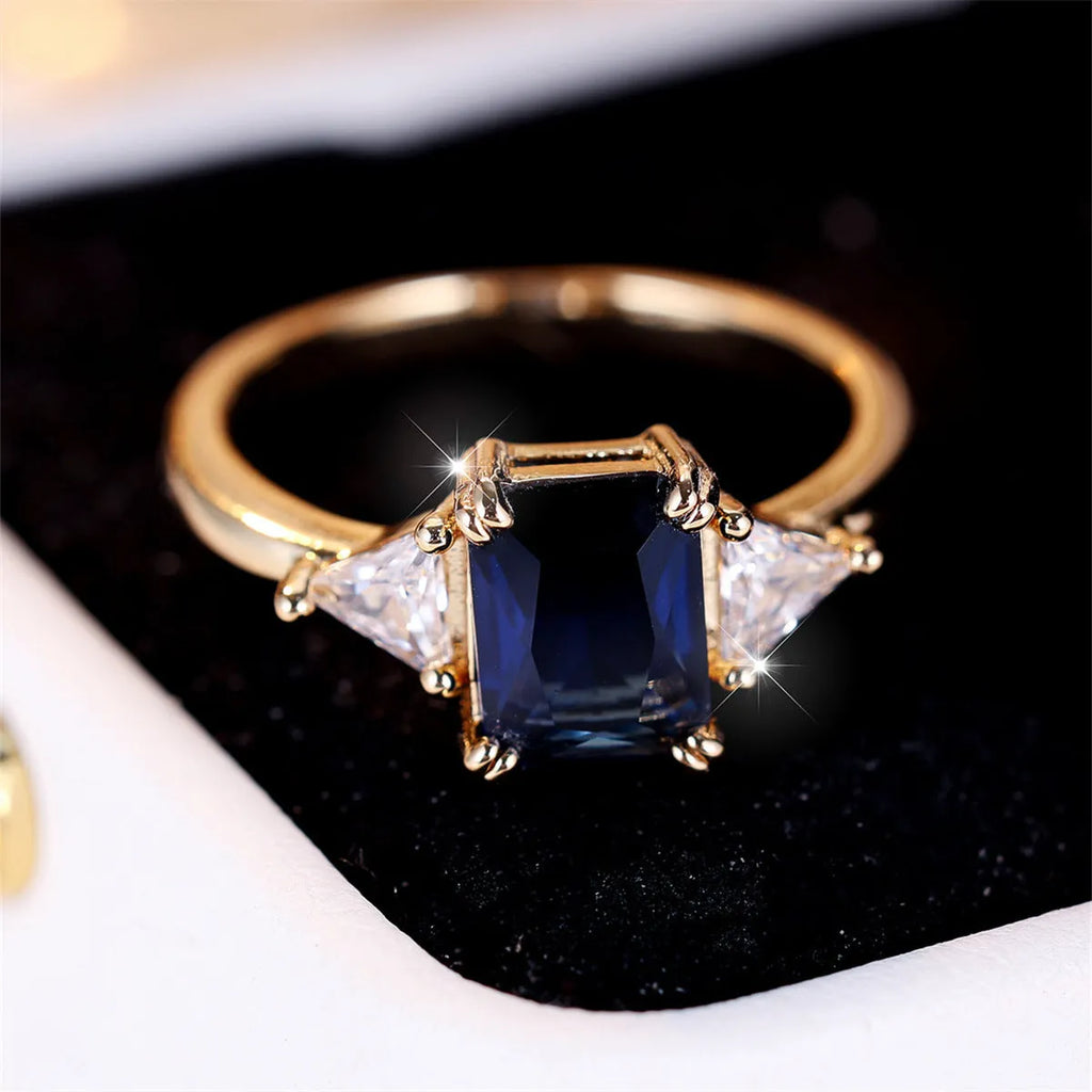Gold and sapphire blue rectangular copper ring for women on a plain background.