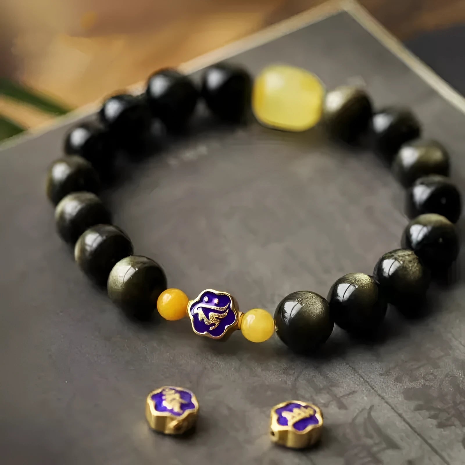 Golden obsidian bracelet with geometric beads and a detailed zodiac animal charm on a wrist.