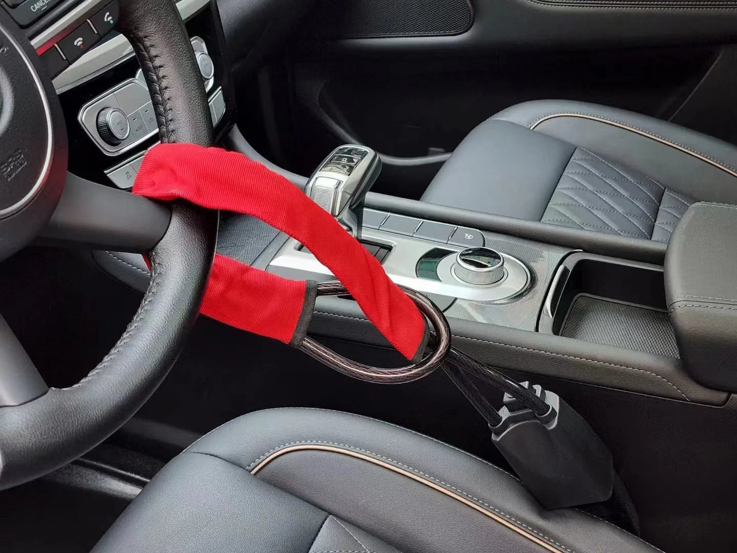 Red steel car steering wheel security lock with coiled cable on a car seat.