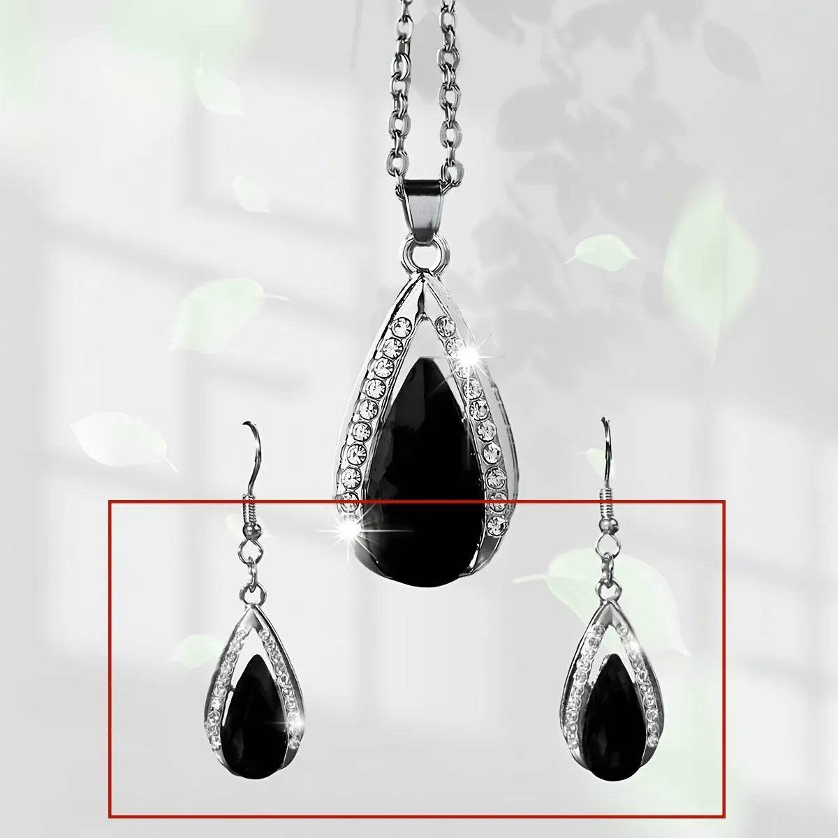 Black and red teardrop-shaped glass pendant necklace and matching earrings set laid flat.