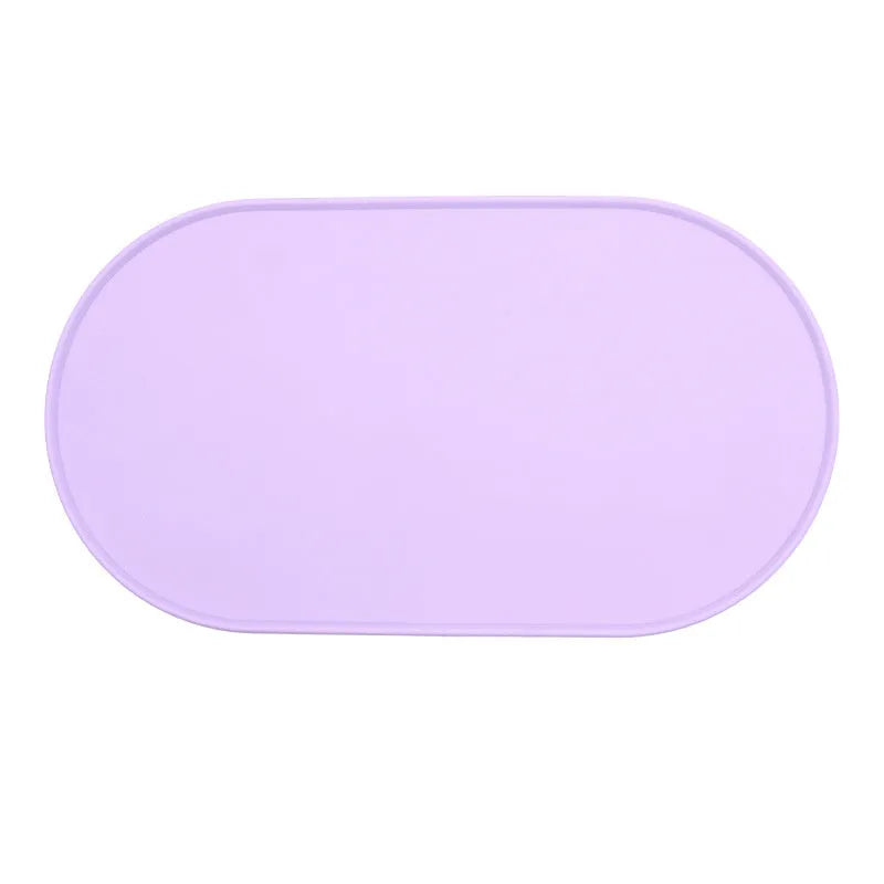 Beige silicone cat feeding mat with raised edge containing a food bowl and scattered kibble on a kitchen floor.