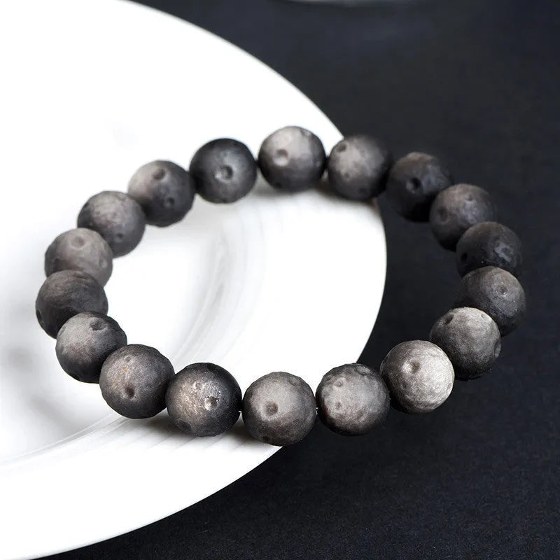 Natural obsidian crater ball bracelet in gold or silver stone colour on a wrist, showing textured bead surface.