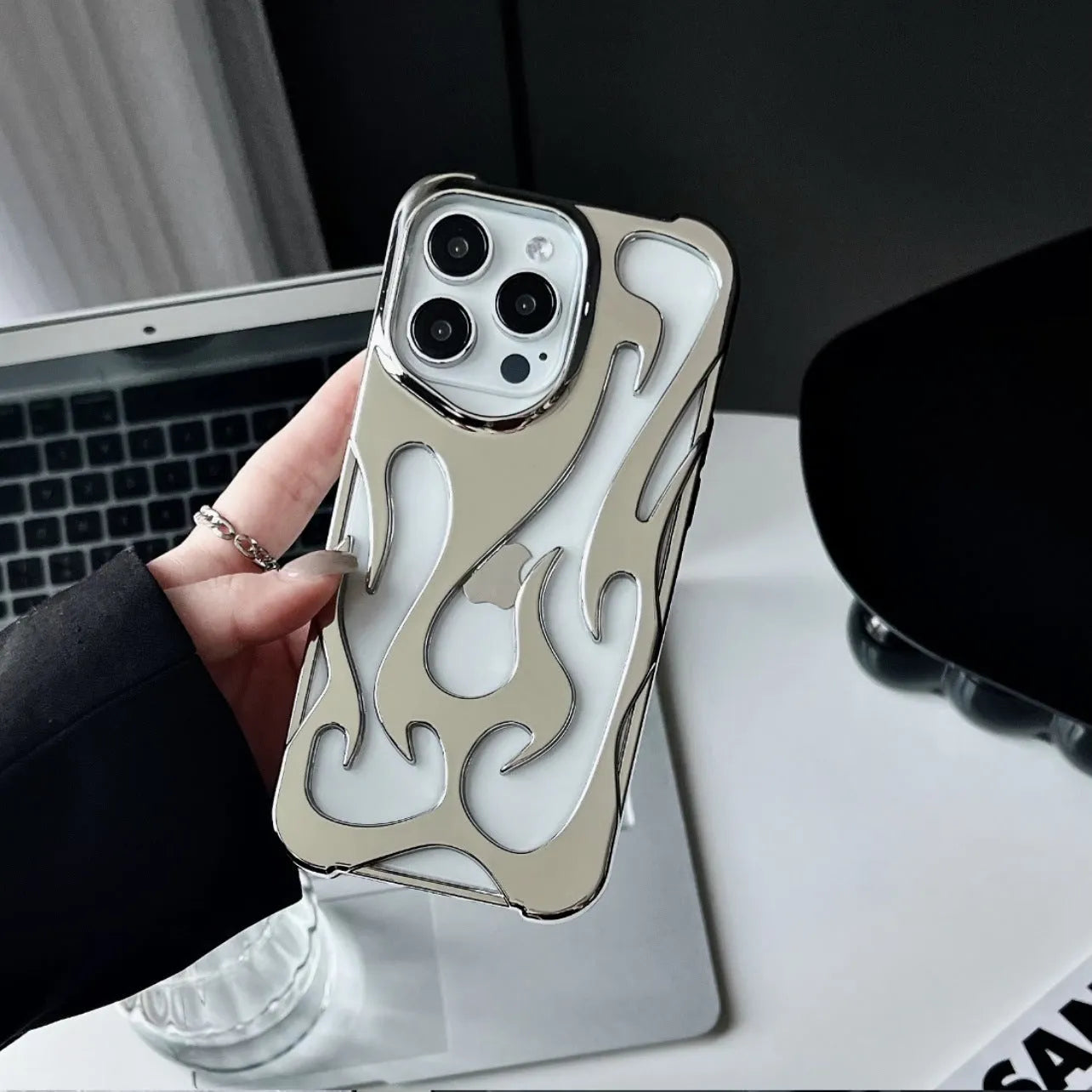 Electroplated hollow flame pattern phone case for iPhone on a table, showing silver metallic finish and cut-out design.