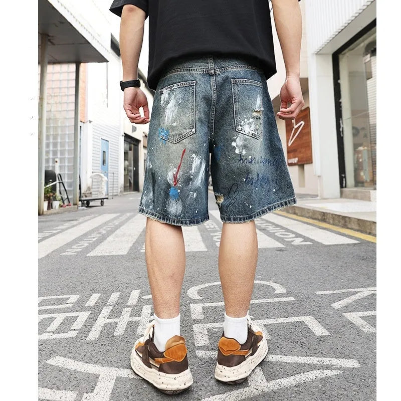 Blue men's ripped denim shorts with graffiti style and straight leg cut on a hanger.