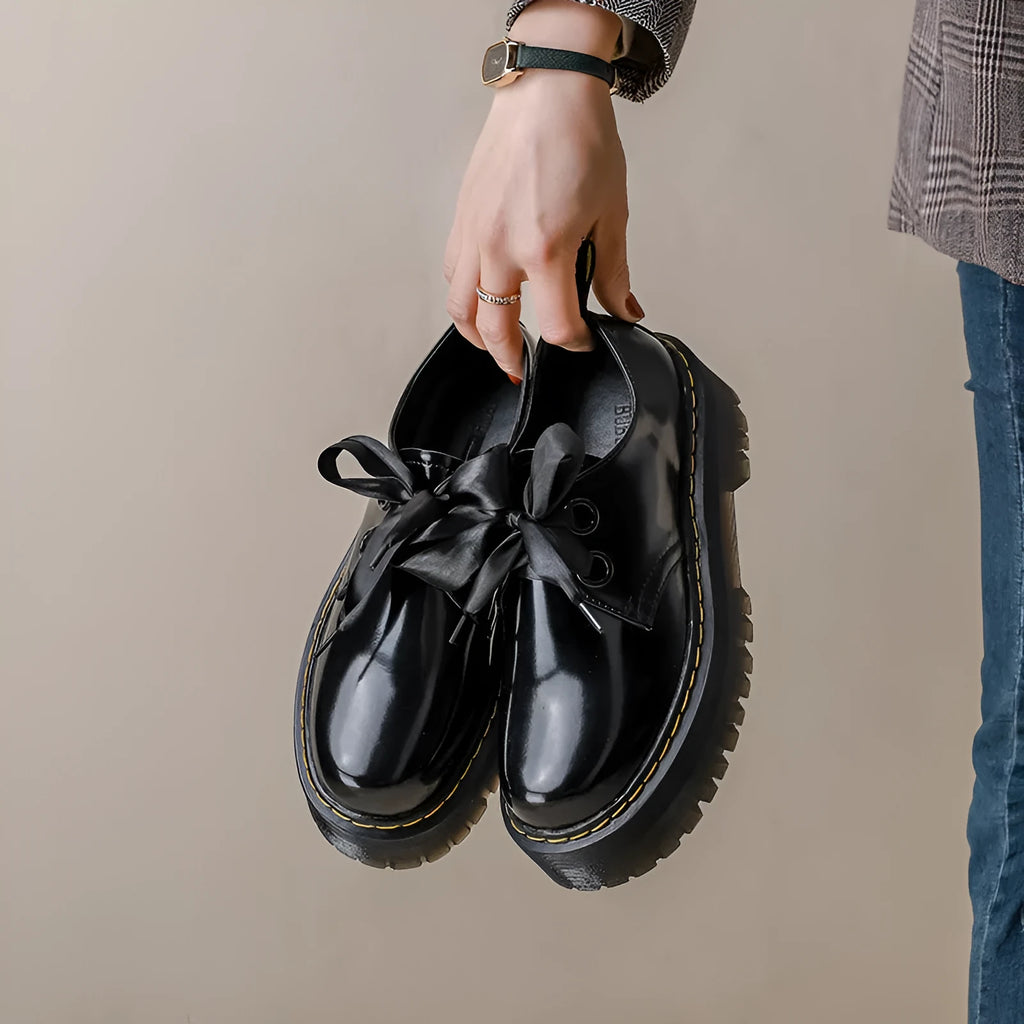 Black women's thick soled lace-up shoes with a cross-strap and ribbon detail on the front.