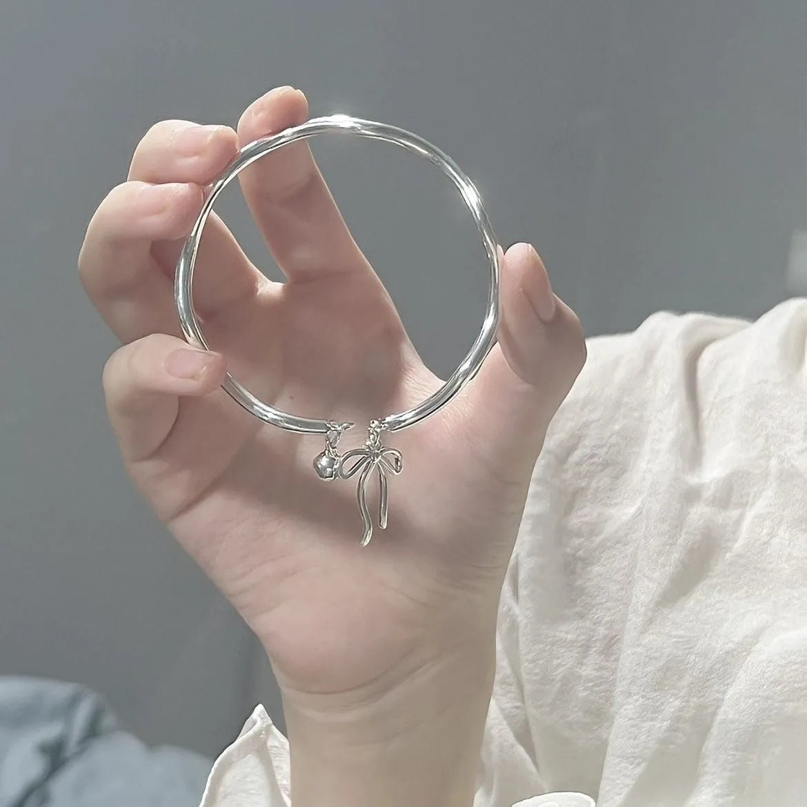 Silver toned adjustable bracelet with bow bell charm on a wrist, showing lobster clasp.
