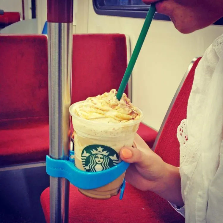 Portable transportation cup holder in red, attached to a bus handrail, holding a coffee cup