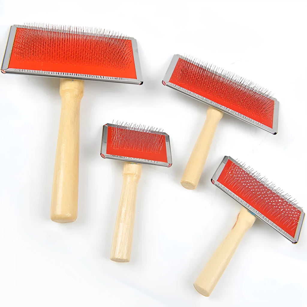 Red pet needle comb with wooden handle and stainless steel pins on a grooming surface