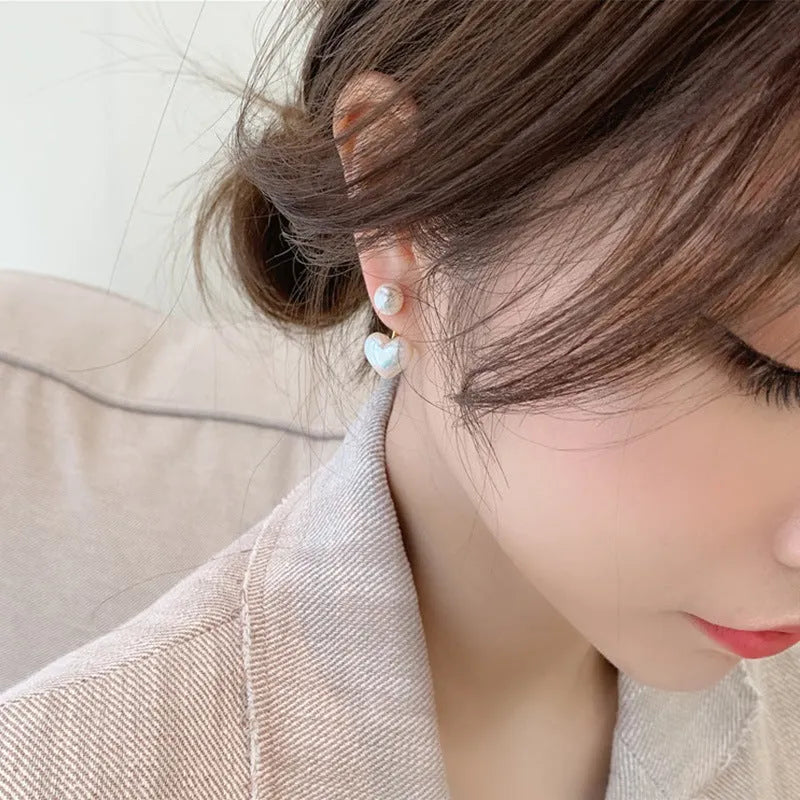 Close-up of women's heart-shaped alloy stud earrings with inlaid pearl-like artificial gems on a white background.