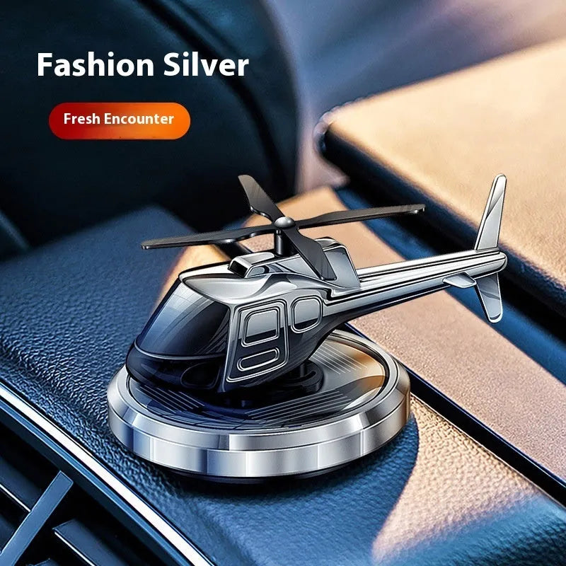 Silver metal solar-powered helicopter car air freshener clipped to a vehicle air vent, with rotating blades.