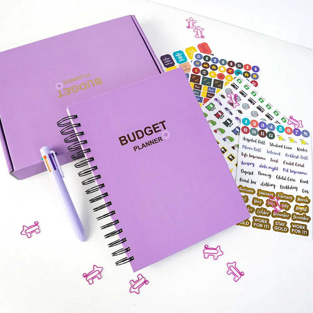 J12 purple coil-bound financial planning notebook with pen, stickers, and paper clips on a desk.