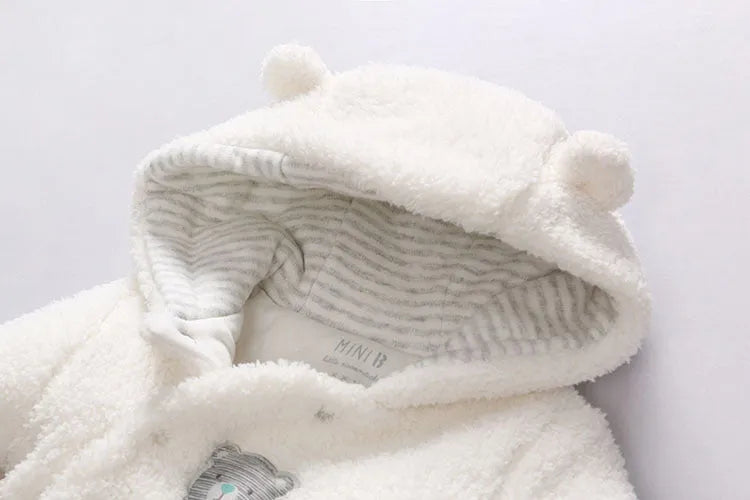 Baby wearing a cotton padded winter jumpsuit with long sleeves, available in marrón, pink, or white colours.