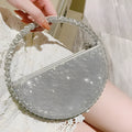 Round silver white PU evening bag with rhinestone details and crossbody strap on flat surface