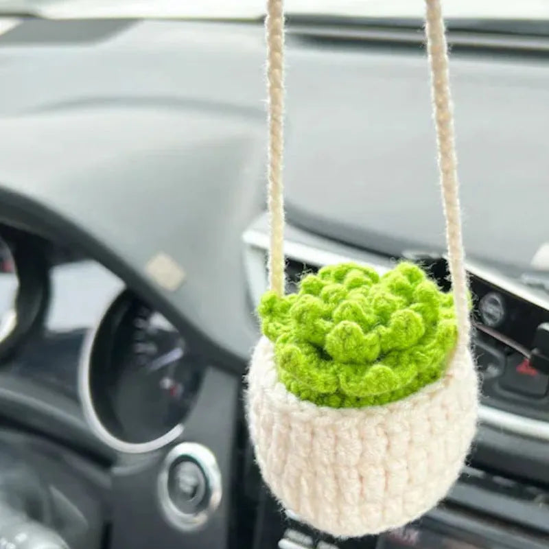 Green and white crocheted wool car plant decoration with a white hanging rope.