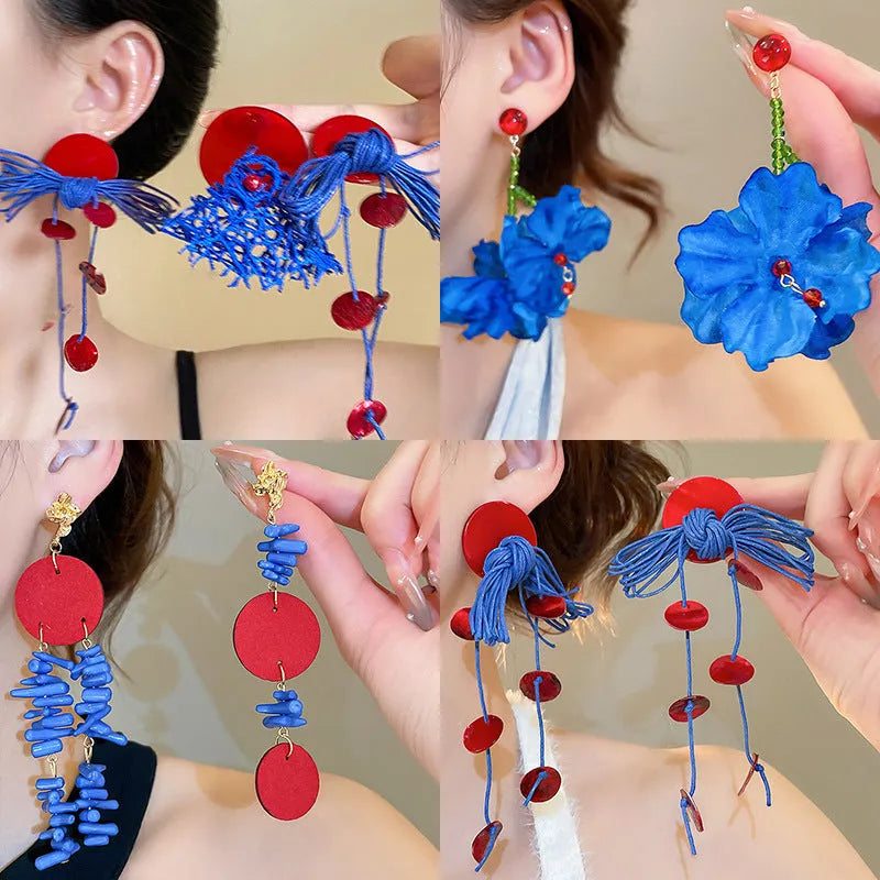 A pair of geometric cloth earrings with a blue resin flower decoration and silver needle detail.