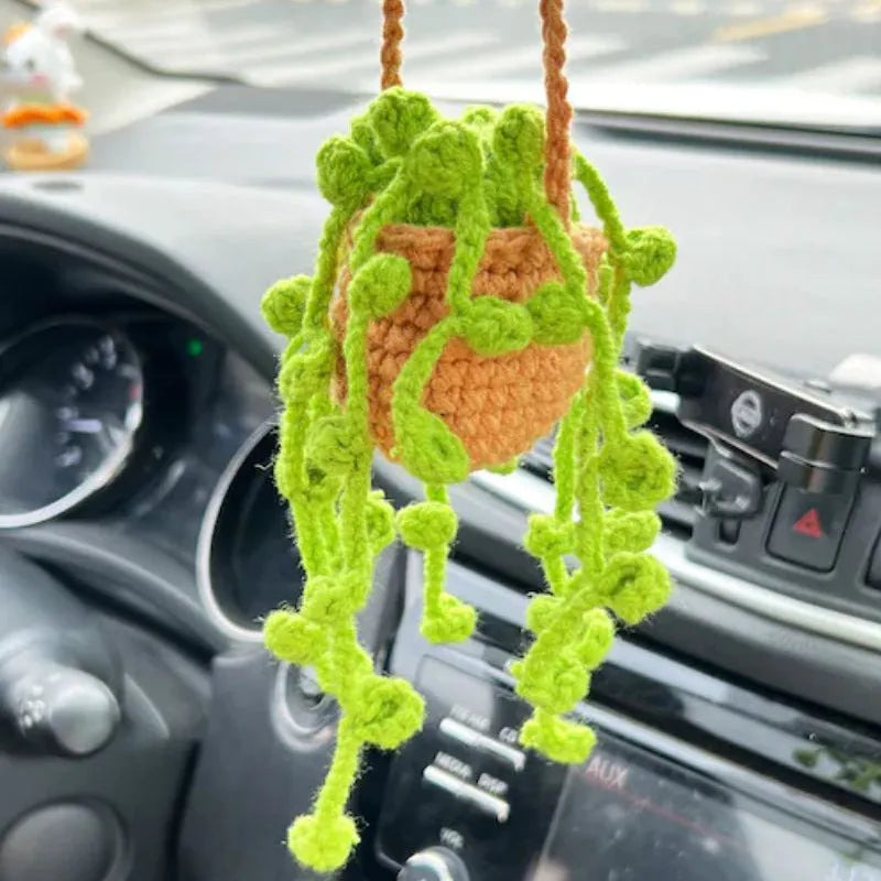 Green and white crocheted wool car plant decoration with a white hanging rope.