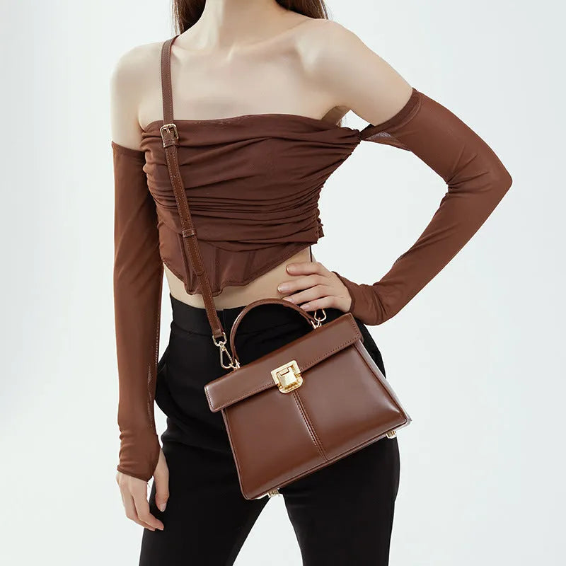 Women's black genuine leather shoulder bag with a clasp, shown with adjustable strap and open to reveal internal zippered pocket.