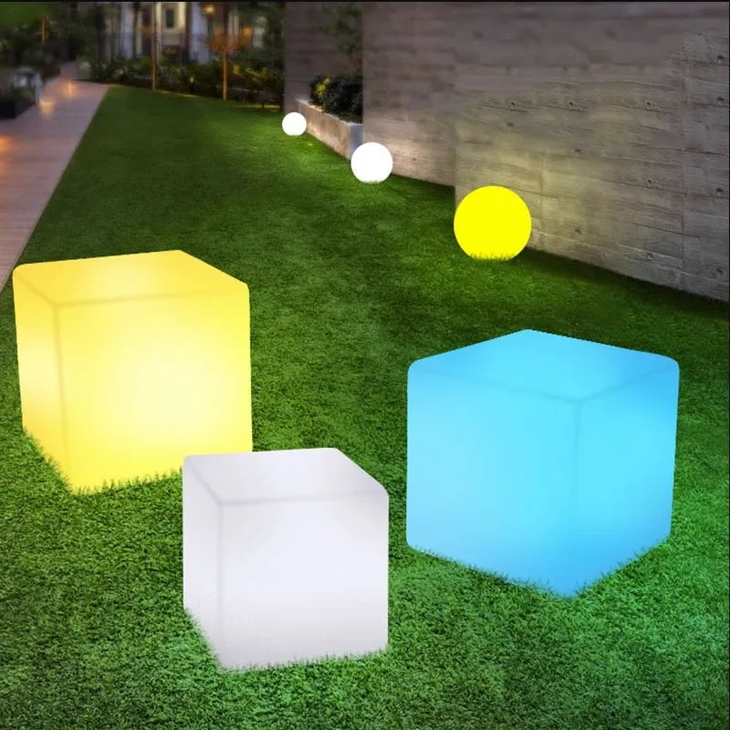 A modern square white LED cube light stool in a garden setting, showing its size options.
