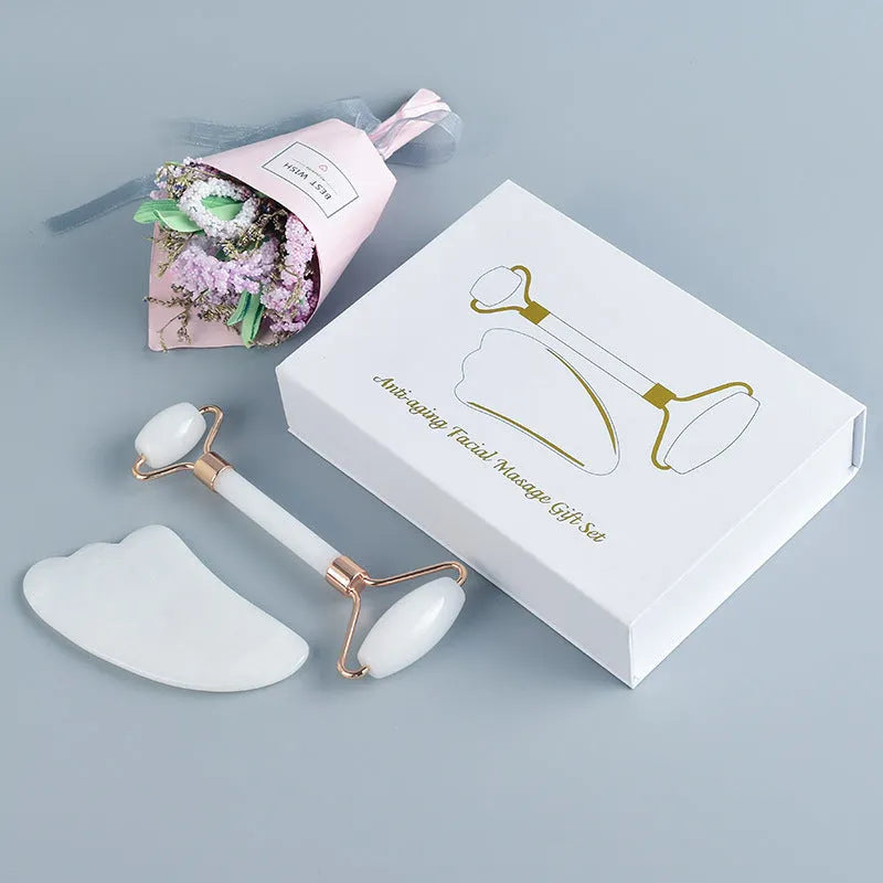 White jade facial roller and gua sha scraping board set on a table.