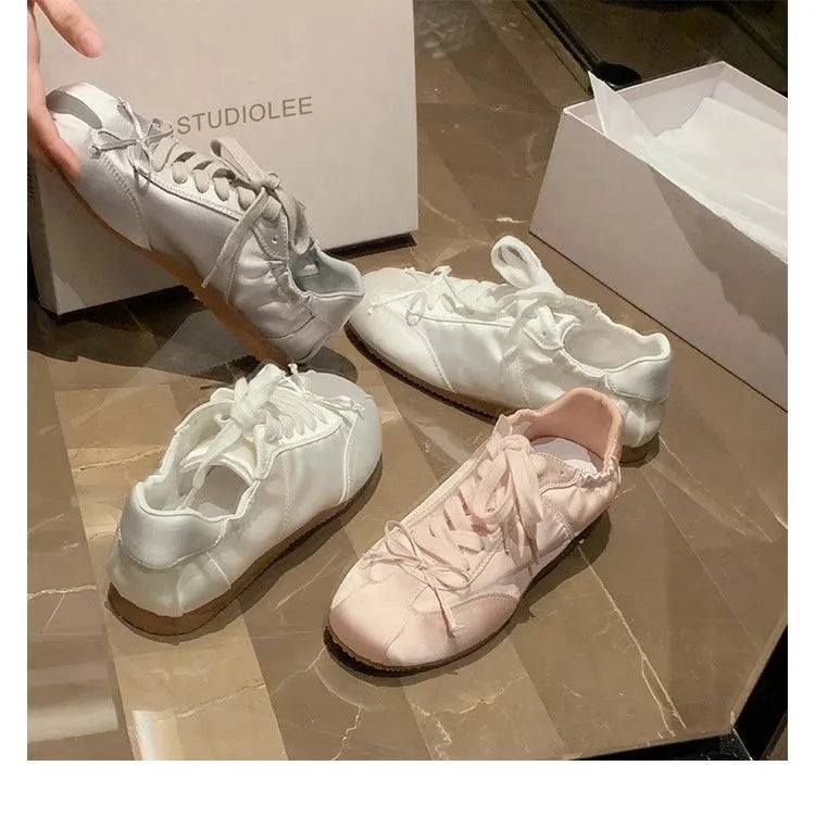 Women's champagne pink satin ballet flat shoes with a round toe and white front lace-up detail.