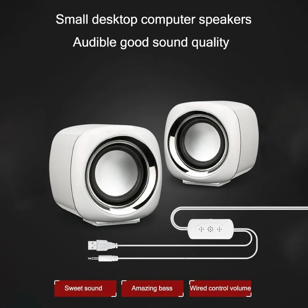 A pair of small black wired computer speakers with a volume scroll wheel, shown next to a 3.5mm audio plug on a desk.
