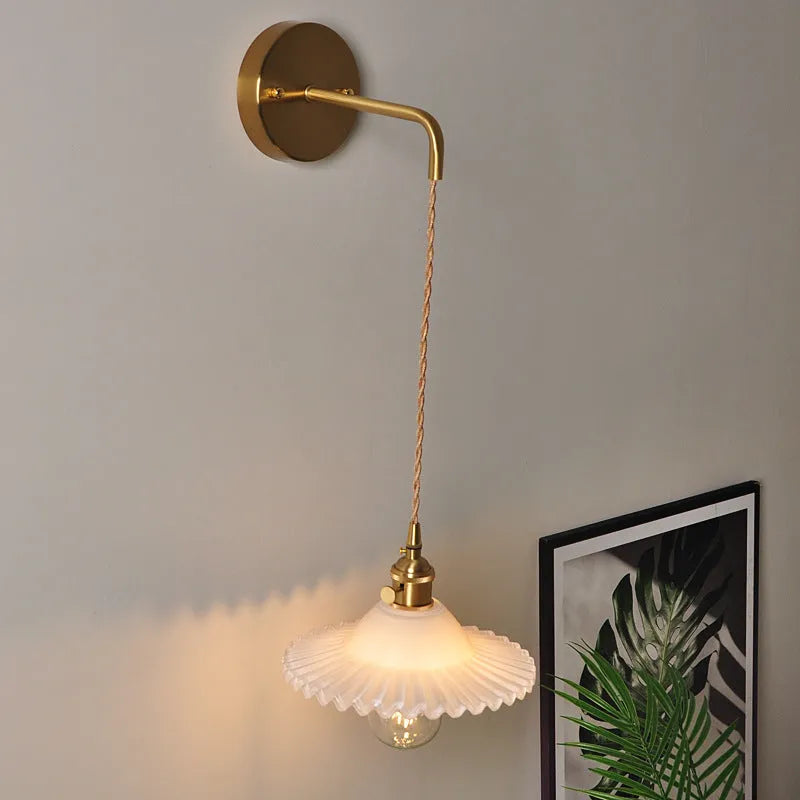 Retro brass wall lamp with a white glass lotus flower shade mounted on a beige wall.