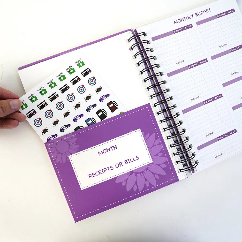 J12 purple coil-bound financial planning notebook with pen, stickers, and paper clips on a desk.