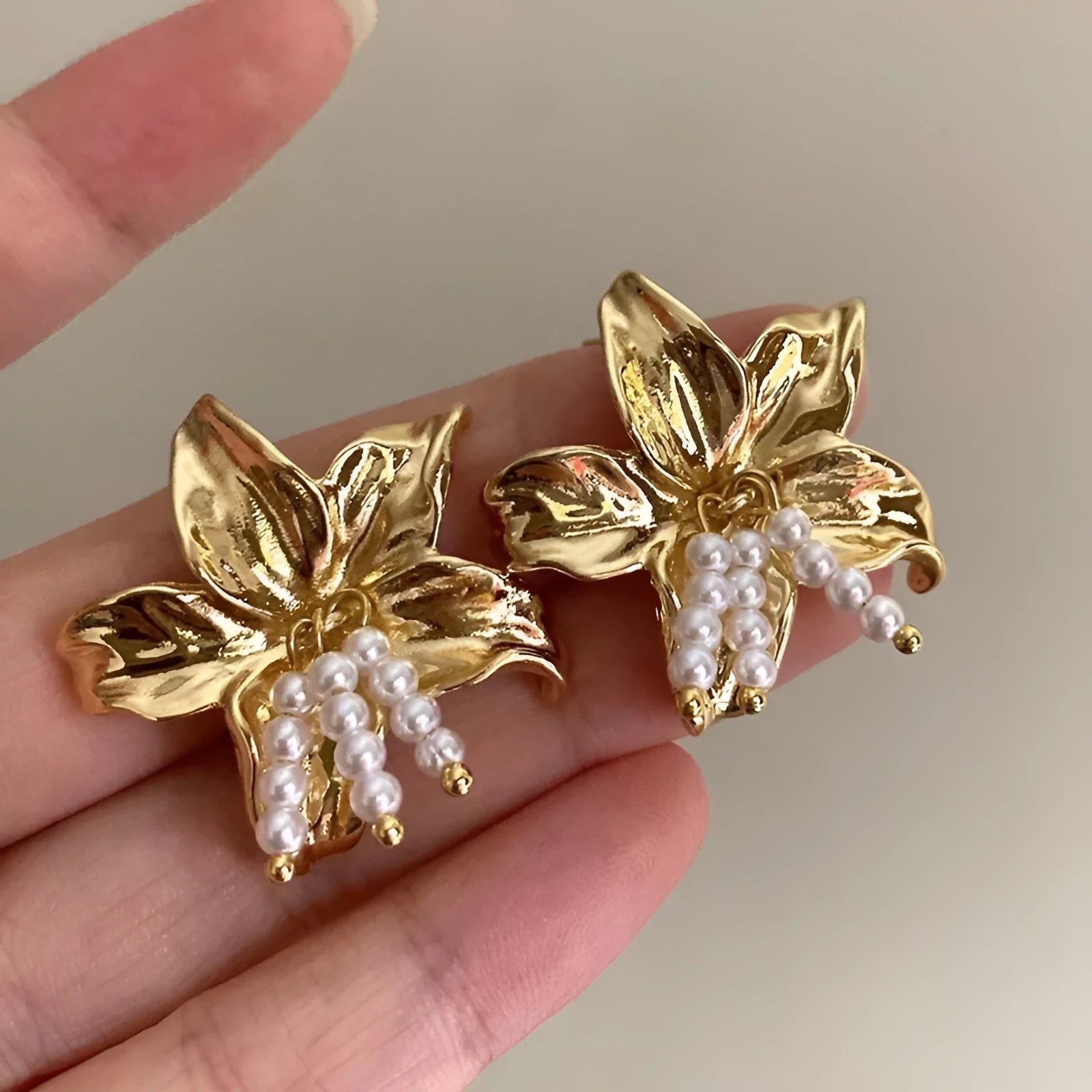 Golden flower-shaped earrings with pearl details on a white background.