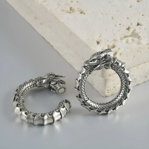 A pair of large, geometric dragon-shaped alloy earrings with an antique silver finish and hollow-out details.
