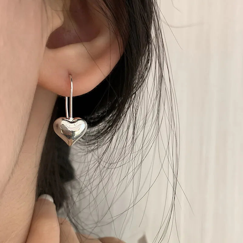 Silver glossy heart-shaped Korean-style earrings with a three-dimensional design on a white background.