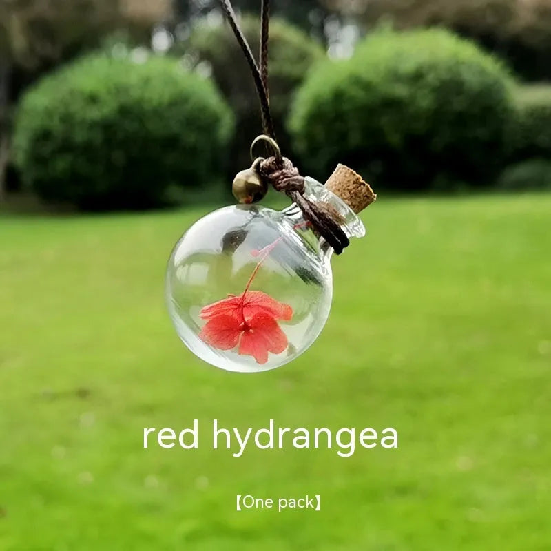 Glass car perfume pendant with preserved flowers inside, shown in a selection of different floral colours.