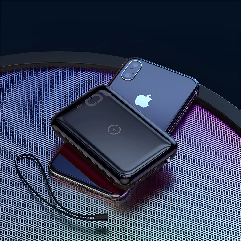 Square black wireless power bank with digital display showing battery percentage, next to a smartphone on its wireless charging surface.