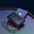 Square black wireless power bank with digital display showing battery percentage, next to a smartphone on its wireless charging surface.