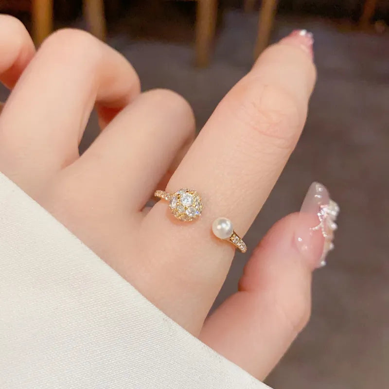 Open-end pearl ring with round zircon stone in gold or silver colour finish.