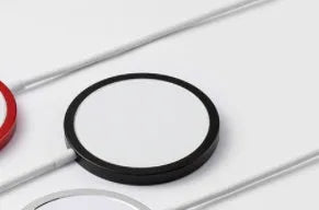 Silver metal Magsafe-compatible magnetic wireless charger for iPhone, shown next to a mobile phone.