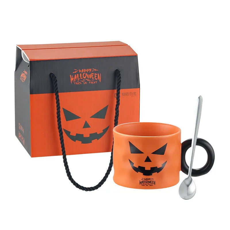 Orange ceramic pumpkin-shaped mug with handle on a table beside a dessert spoon and gift box.